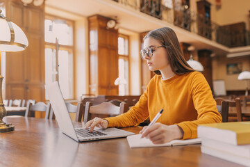 In the Library - A pretty student with a laptop and books works in the library of a high school or...