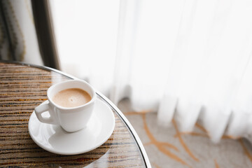 cup of hot coffee on table besides window