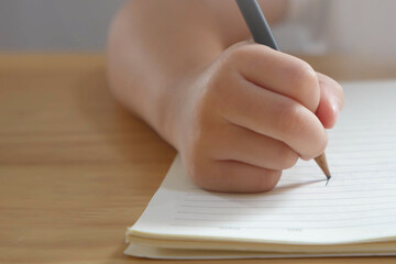 Kid hand writing with pencil in a book on wooden table