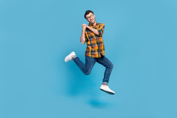 Fototapeta na wymiar Full length portrait of overjoyed cheerful man jump arms hold empty space isolated on blue color background