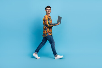 Fototapeta na wymiar Full length profile photo of cheerful person walking use netbook isolated on blue color background