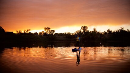 Silhouette of a young woman standing on the Sup board in the sunset lake