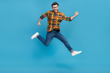 Obraz premium Full size photo of astonished delighted guy jumping raise fists triumph isolated on blue color background