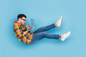 Full body profile portrait of falling flying person use wireless netbook isolated on blue color background © deagreez
