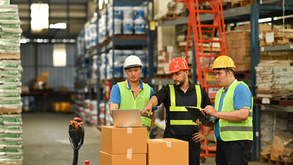 Manager and warehouse worker inspecting stock tick and cardboard stock product on laptop computer in a large warehouse