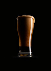 A glass of dark beer on a black background.