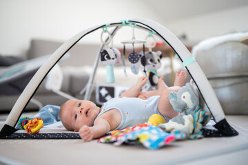 Cute baby boy playing with hanging toys arch on mat at home Baby activity and play center for early...