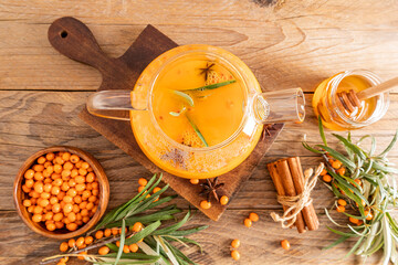 autumn composition of the tea ceremony. a large glass teapot with sea buckthorn tea, honey in a jar, berries in the bowl. top view. wooden background.
