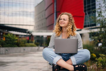 Front view of a happy student girl wearing eyeglasses, smiling sitting with laptop, surfing the net to preparing for exams. Distance learning, online education