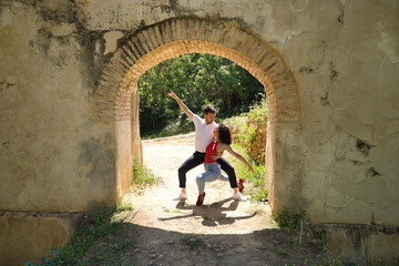 Attractive young couple dancing sensual bachata under an ancient stone arch in an outdoor park. Latin, sensual, folkloric, urban dance concept.