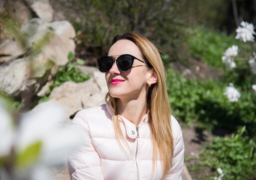 portrait of a smiling blonde woman in sunglasses sitting on the stones in spring park 