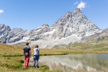 Rear view of a mother carrying her toddler on a baby wrap carrier, joint the father while are looking at Matterhorn during a hiking day at Italian alps.