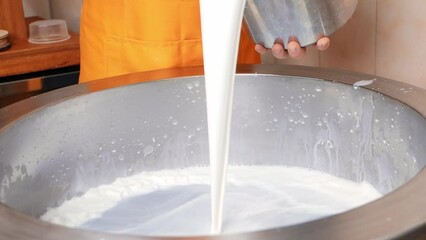man pours milk into vat for cooking, process of making cheese. slow motion