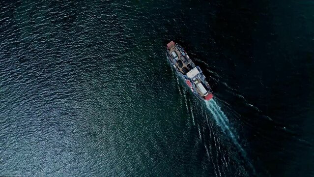 4k Top view of ship with cargo moves on water outdoors irrl. Aerial picture of long vehicle with cars on dock moving along blue sea on summer day. Tourist uses flying drone in countryside and takes
