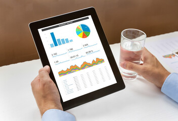 Hands holding a digital tablet with analytical data and a glass of water.