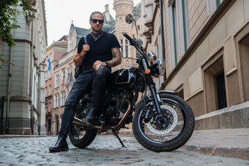 Fototapeta na wymiar Portrait of attractive man biker with tattooes posing on his motorcyle in alleyway downtown.