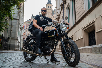 Fototapeta na wymiar Shot of trendy male biker looking like rocker riding motorcyle in city.