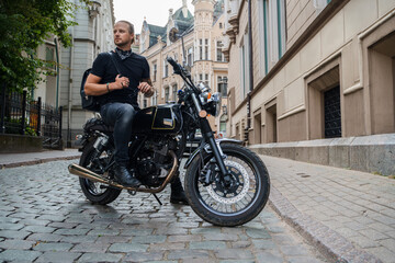 Obraz na płótnie Canvas Shot of trendy male biker looking like rocker riding motorcyle in city.