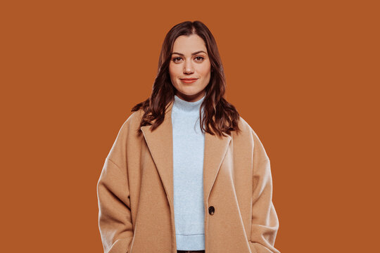 Portrait of beautiful smiling girl in beige coat joyfully looking at camera isolated over beige background.