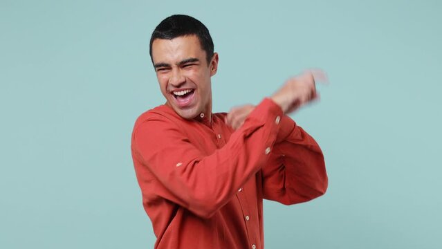 Young middle eastern man wear red shirt dance clench fists waving rising expressive gesticulating hands fooling around have fun enjoy celebrate play isolated on plain pastel light blue cyan background