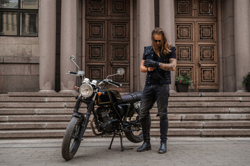 Portrait of guy motorcyclist dressed like rocker wearing protective gloves.