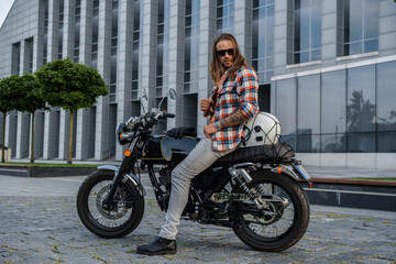 Plakat Shot of trendy guy with long hairs driving motorcycle outdoors in daytime.