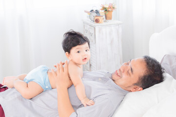 Obraz premium Selective focus happy father playing with 1-2 months newborn baby with love on bed at home, Asian dad and adorable infant have fun enjoy lying down together. Family relationship with toddler concept.
