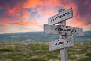 feasability desirability viability text quote on wooden signpost up on the mountains during sunset and red dramatic skies.