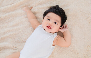 Selective focus Asian newborn baby age 2-3 months lying down alone on bed and looking camera,...