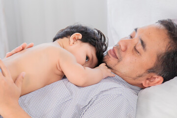 Obraz na płótnie Canvas Selective focus Healthy asian father lying on bed with newborn baby. Adorable infant lying on daddy chest with safe and love. Dad and toddler have fun enjoy lying down together in holiday.