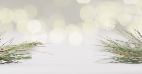 Image of close up of bokeh christmas fairy lights and pine tree branches on grey background