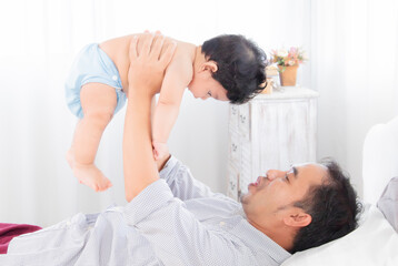 Fototapeta na wymiar Selective focus asian father play and tease with newborn baby in bedroom. Dad holding lifting toddler on bed with fun and tender. Adorable little boy having fun with daddy togerther at home.