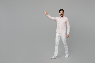 Fototapeta na wymiar Full body young caucasian man 20s he wear basic white shirt walking going point index finger aside on workspace area mock up isolated on plain grey background studio portrait People lifestyle concept