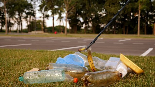 A close-up of an activist collecting garbage with tongs in an urban area, plastic garbage and a banana skin.