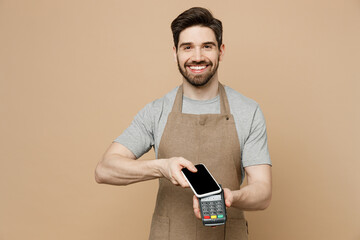 Young man barista barman employee in brown apron work in coffee shop hold mobile phone with blank...