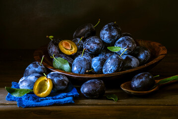 Ripe blue Fresh organic  sweet plums just picked from the tree, walnut wood bowl plate indoors. Autumn Harvest of fruits  rustic  wooden dark black background leaf clay.