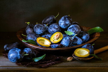 Ripe blue Fresh organic  sweet plums just picked from the tree, walnut wood bowl plate indoors. Autumn Harvest of fruits  rustic  wooden dark black background leaf clay.