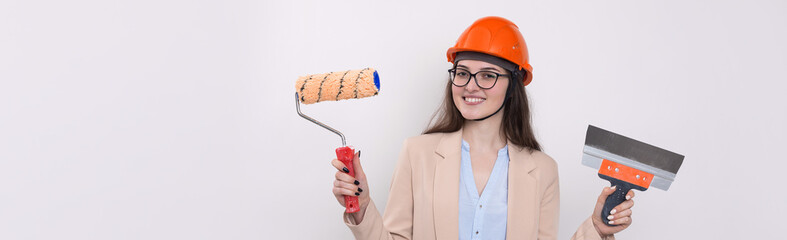 Girl engineer in an orange construction helmet with plastering painting tools in her hands on a white background.