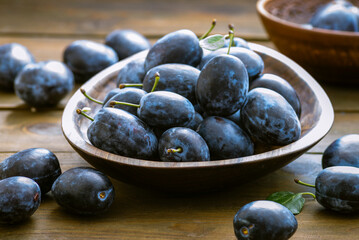 Ripe blue Fresh organic  sweet plums just picked from the tree, walnut wood bowl plate indoors. Autumn Harvest of fruits  rustic  wooden dark black background leaf clay.