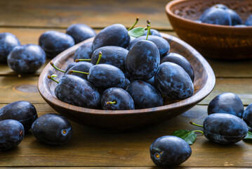 Ripe blue Fresh organic  sweet plums just picked from the tree, walnut wood bowl plate indoors. Autumn Harvest of fruits  rustic  wooden dark black background leaf clay.