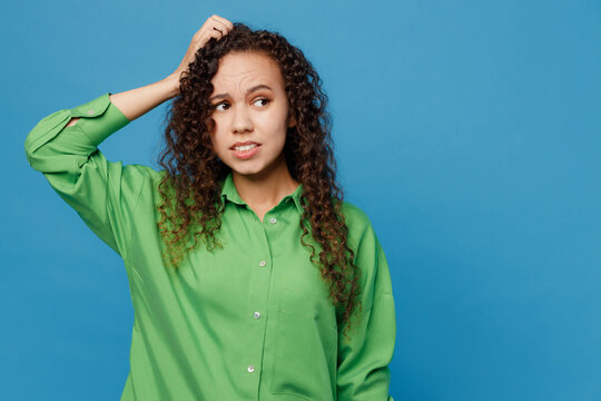 Young minded confused mistaken sad woman of African American ethnicity 20s she wear green shirt look aside hold scratch head isolated on plain blue background studio portrait People lifestyle concept