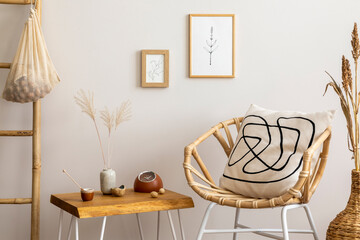 Creative composition of elegant and boho living room with rattan armchair, mock up photo frames, coffee table, dried flower in vase and personal accessories. Cozy home decor. Template.