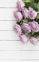 a bouquet of beautiful purple roses on a white wooden background top view