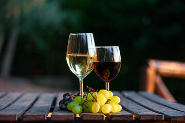 Glasses of red and white wine and grapes on a wooden table outdoor. Wine tasting concept. Copy...