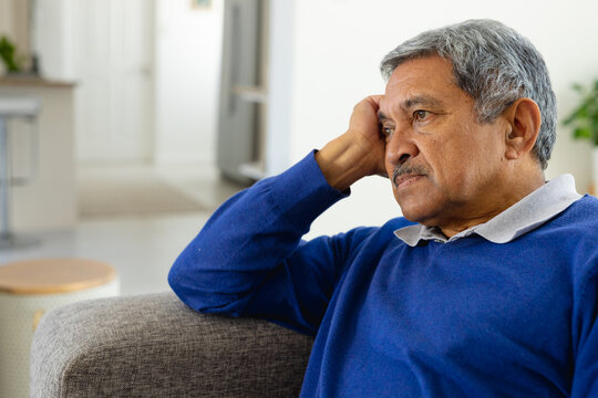 Tired, depressed senior biracial man sitting on couch in living room leaning head on hand