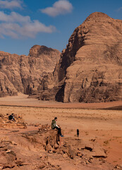 Man sitting on the edge of the rock admiring the desert canyon in the Wadi Rum desert, Jordan