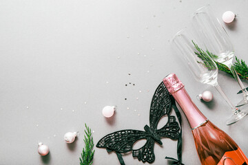 A bottle of champagne, glasses, Christmas balls and a fancy mask on a light gray background. New...