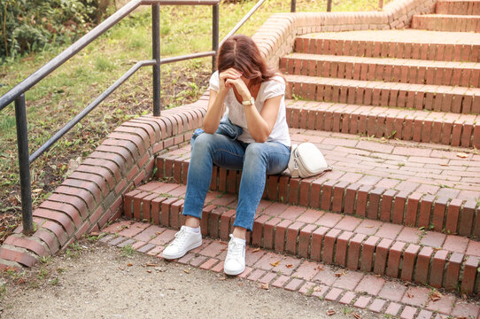 An upset sad young woman sits on the stairs with her head propped up in her hands, the woman is sad, trouble has happened, to yearn and be offended.
