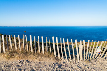 Wooden fence of the famous hiking track named "GR34" in Brittany, France, close to the cliffs of "Cap de la chevre" (Cape of the goat). Blue waters of the atlantic ocean on the background.