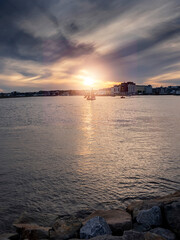 Naklejka premium Silhouette of Galway hooker type wooden boat sailing from harbor at stunning sunset time. Hobby and water sport. Dark and moody sky and dark water of Galway bay, Ireland.